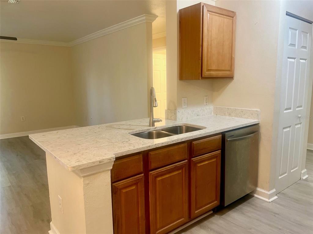 A kitchen features wood cabinets, a stainless steel dishwasher, and a light-colored stone countertop — 18335 BRIDLE CLUB DRIVE UNIT 18335, TAMPA, FL