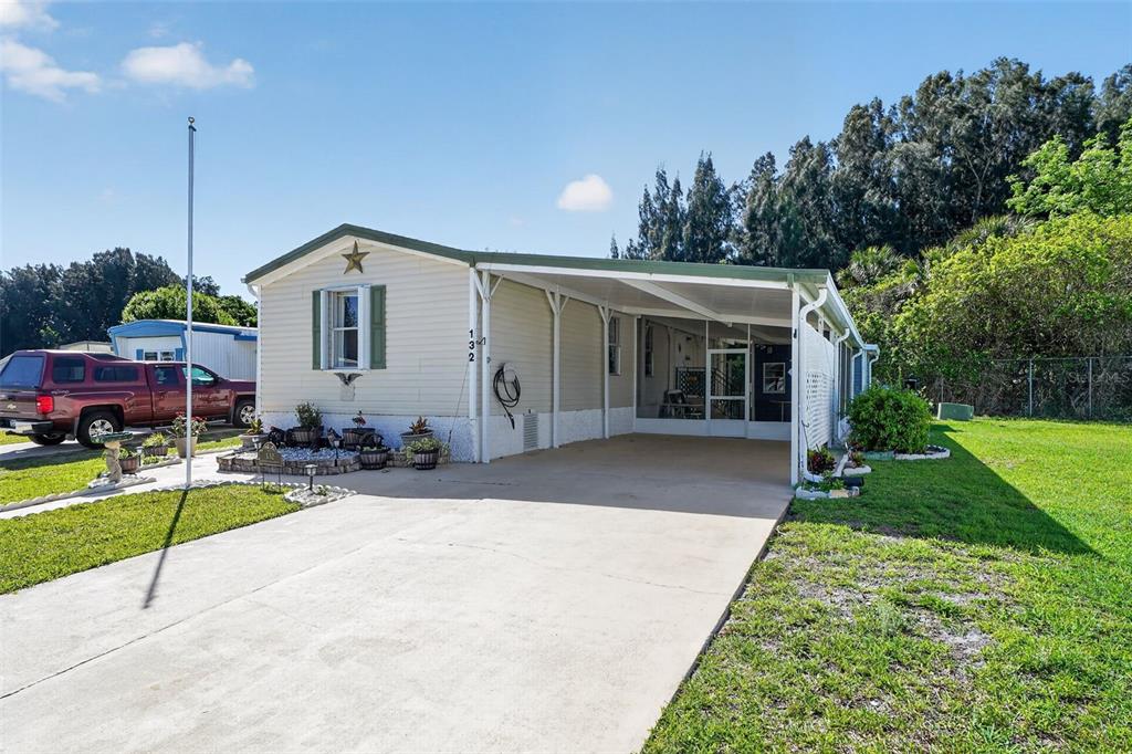 A single-story manufactured home with a concrete driveway, carport, and a small front garden — 132 HOLIDAY PARK BOULEVARD NE, PALM BAY, FL