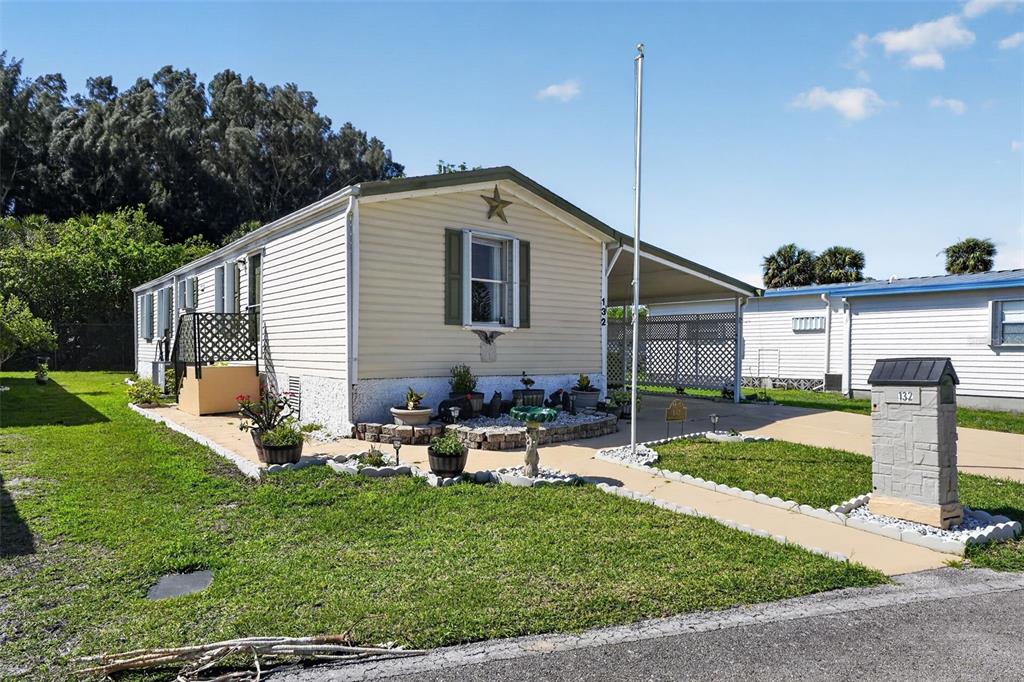 A light-colored mobile home with a carport, a small front garden, and a mailbox — 132 HOLIDAY PARK BOULEVARD NE, PALM BAY, FL