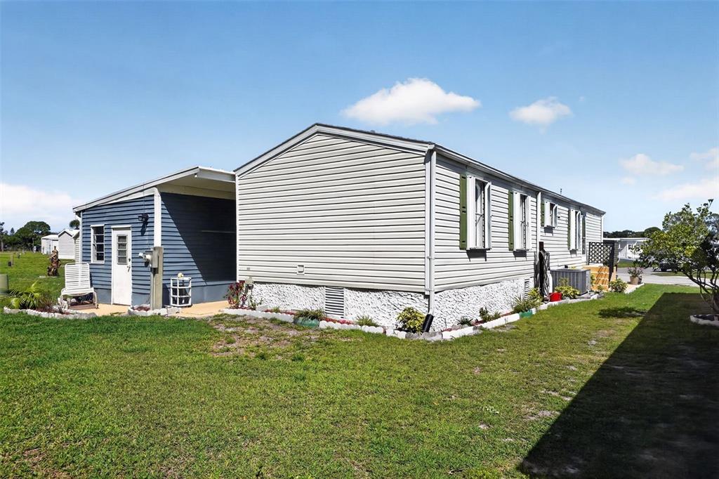 The exterior of a light-colored manufactured home with a side carport and grassy yard — 132 HOLIDAY PARK BOULEVARD NE, PALM BAY, FL