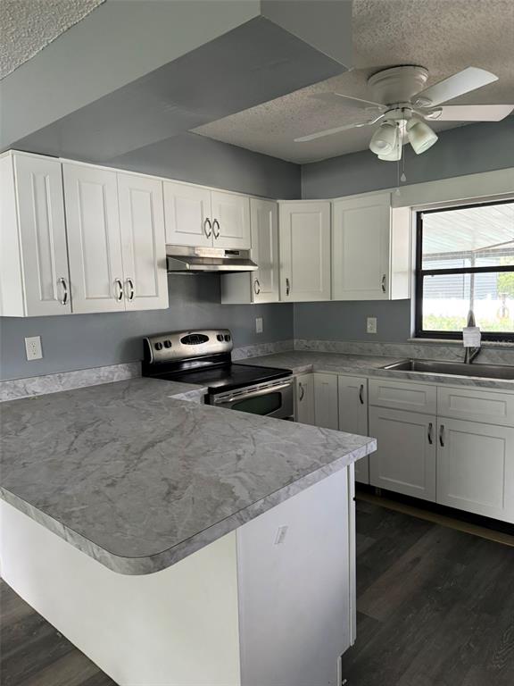 A kitchen features white cabinets, gray marble-look countertops, stainless steel appliances, and dark flooring — 38745 CAMBRIDGE DRIVE, ZEPHYRHILLS, FL