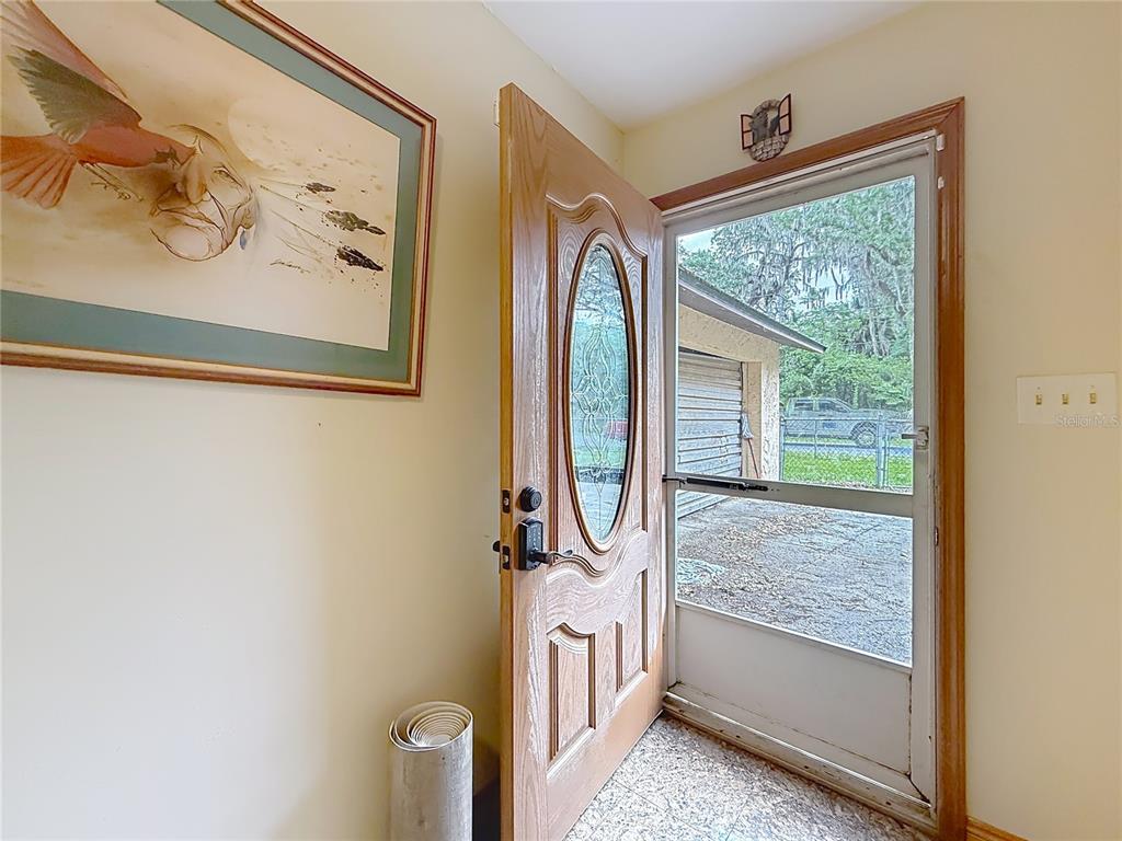 An open front door reveals a view of a driveway, a garage, and trees outside — 2548 CR 422, LAKE PANASOFFKEE, FL