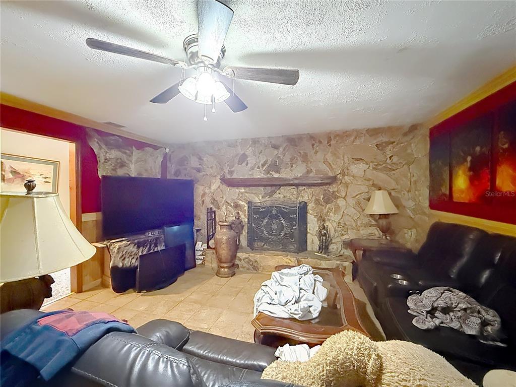 A living room features a stone fireplace, tile flooring, a ceiling fan, and leather furniture — 2548 CR 422, LAKE PANASOFFKEE, FL