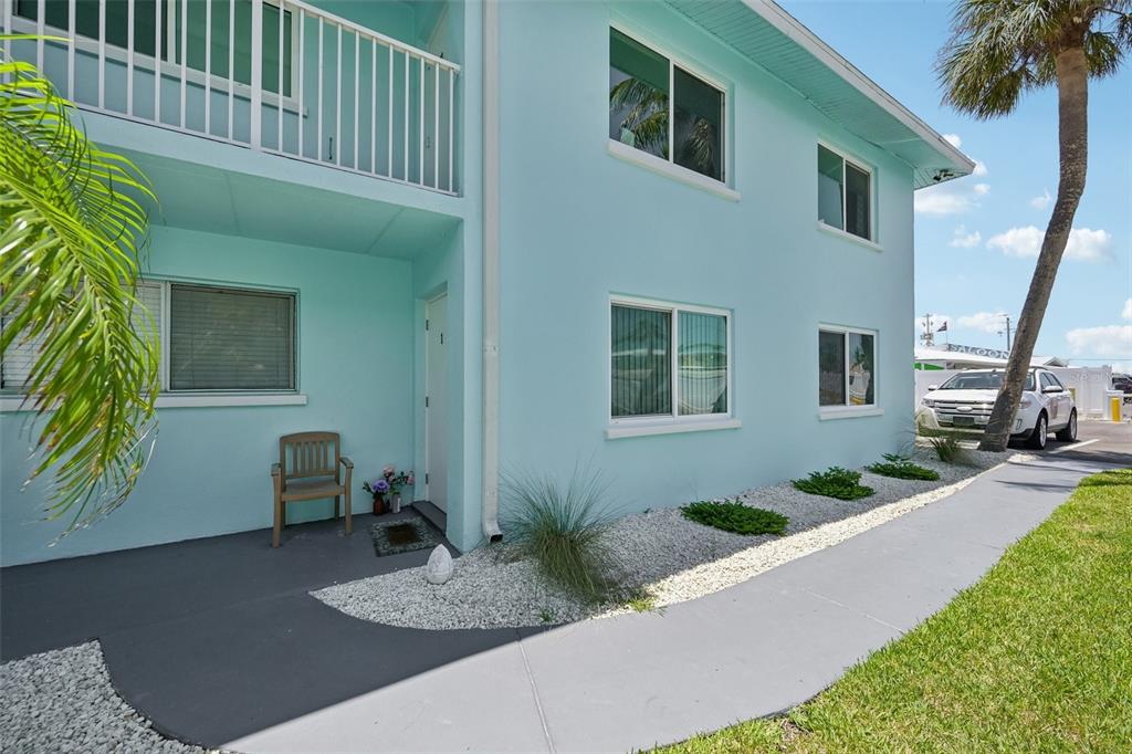 A light blue two-story building features a ground-level patio, white trim, and gravel landscaping — 117 7TH STREET N UNIT 1, BRADENTON BEACH, FL