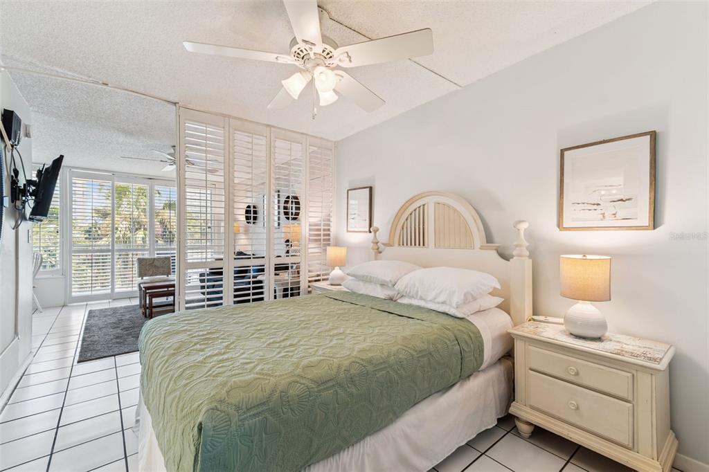 A bedroom features a bed with a green quilt, white furniture, and sliding shutter doors — 800 BAYWAY BOULEVARD UNIT 17, CLEARWATER BEACH, FL