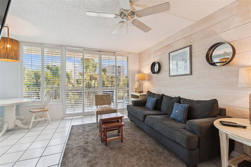 A living room features a dark sofa, wood-paneled wall, tiled floors, and sliding glass doors — 800 BAYWAY BOULEVARD UNIT 17, CLEARWATER BEACH, FL