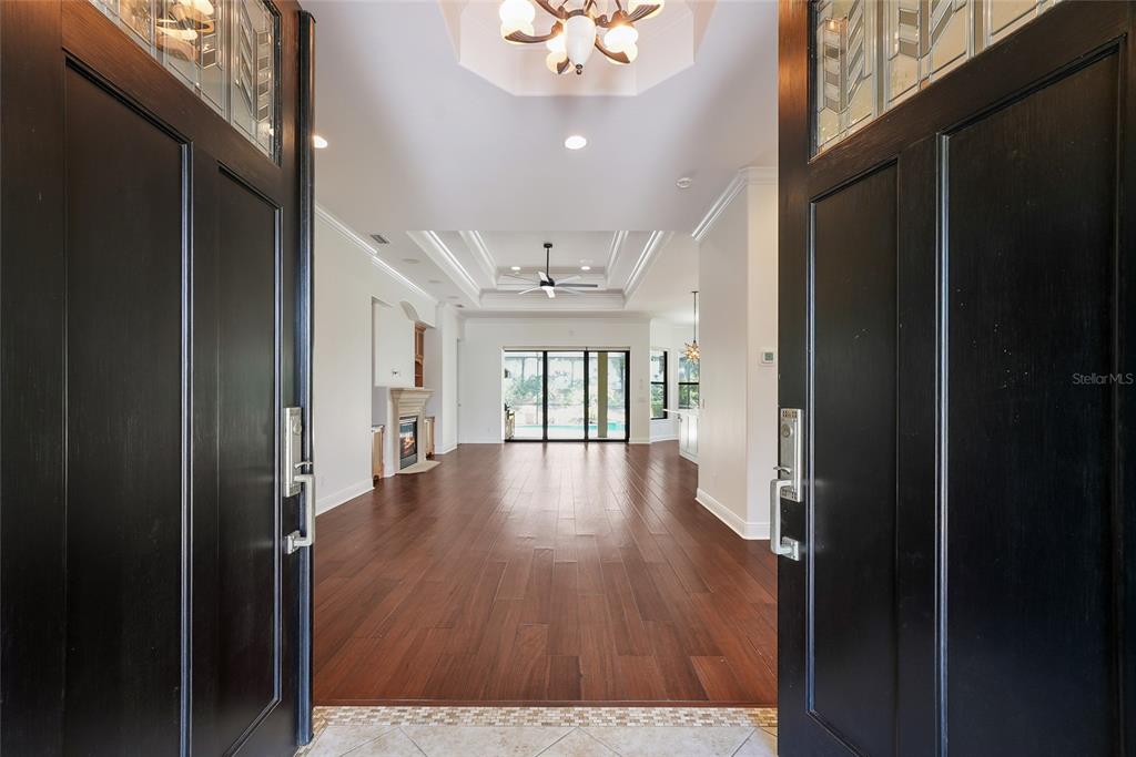 A view through open double doors into a living room with hardwood floors and tray ceilings — 15308 HELMSDALE PLACE, LAKEWOOD RANCH, FL