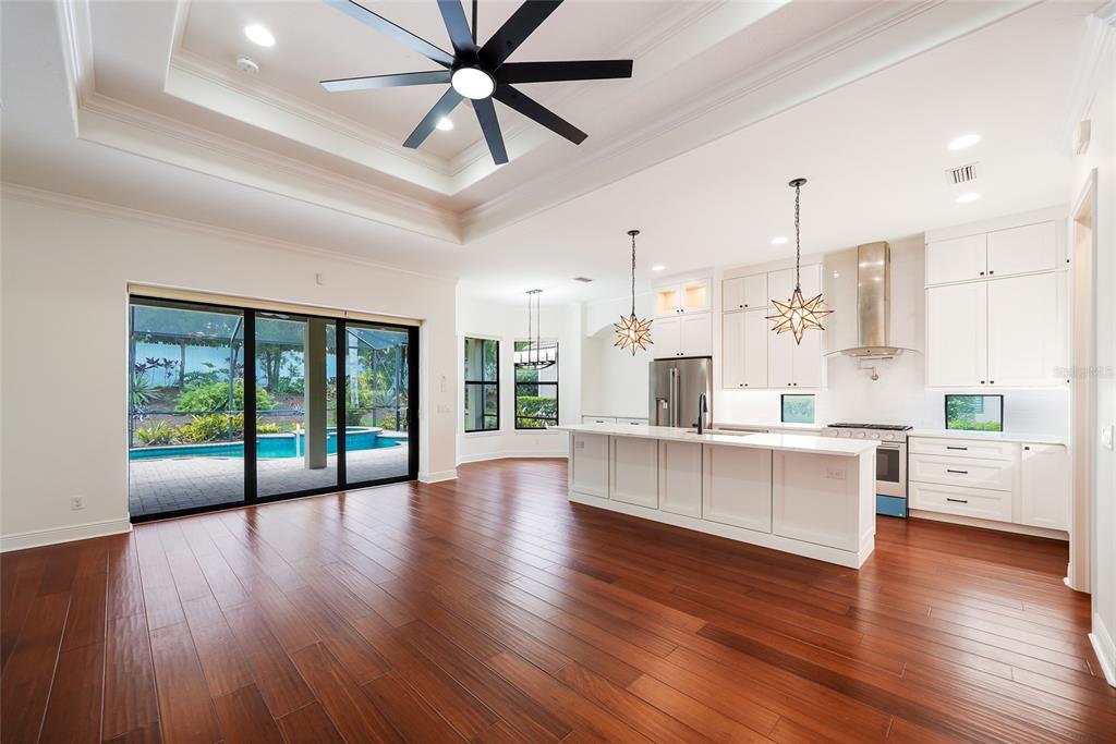 A kitchen and living area with white cabinetry, a large island, and hardwood floors — 15308 HELMSDALE PLACE, LAKEWOOD RANCH, FL