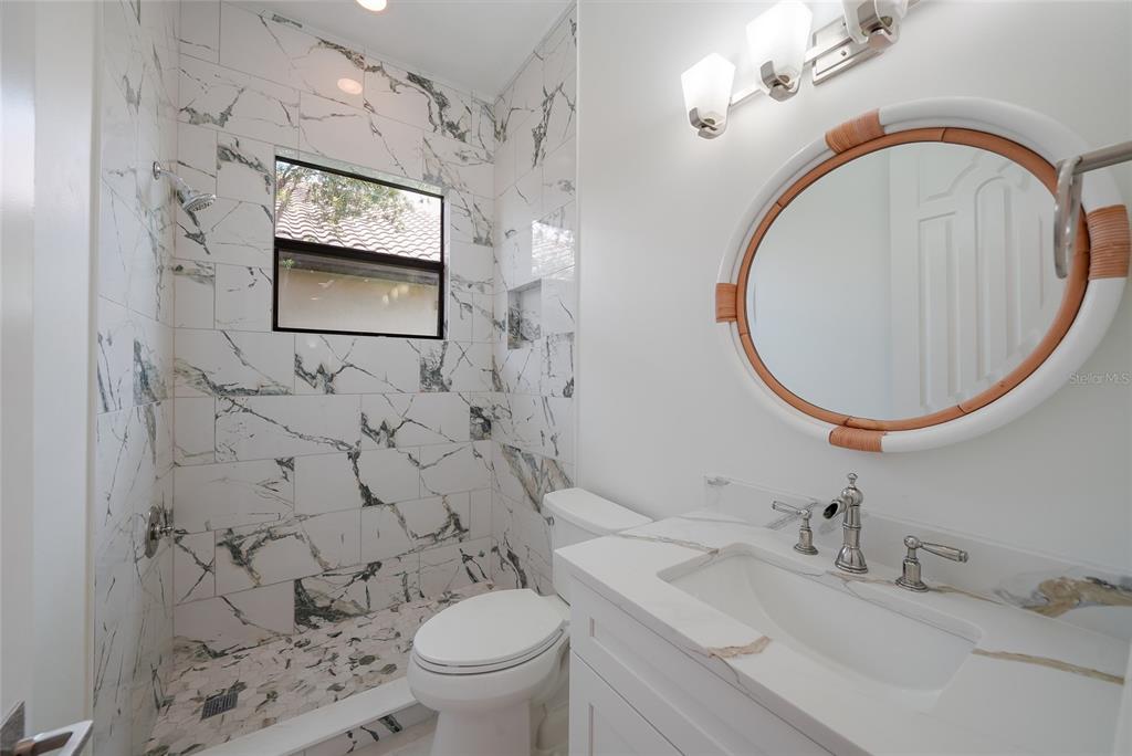 A bathroom features a marble-tiled walk-in shower, a white vanity, and a round rattan mirror — 15308 HELMSDALE PLACE, LAKEWOOD RANCH, FL