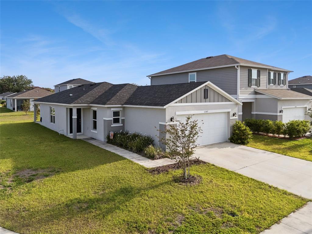A single-story house with a white garage and gray siding stands next to a two-story home — 1247 PAPAYA CIRCLE, DAVENPORT, FL