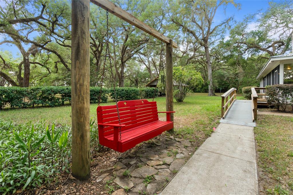 A bright red wooden porch swing hangs from a wooden frame in a grassy yard — 1153 CR 722, WEBSTER, FL
