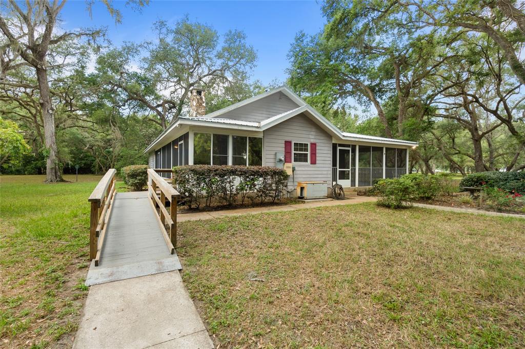 A gray house with a screened porch and a wooden wheelchair ramp in a yard — 1153 CR 722, WEBSTER, FL