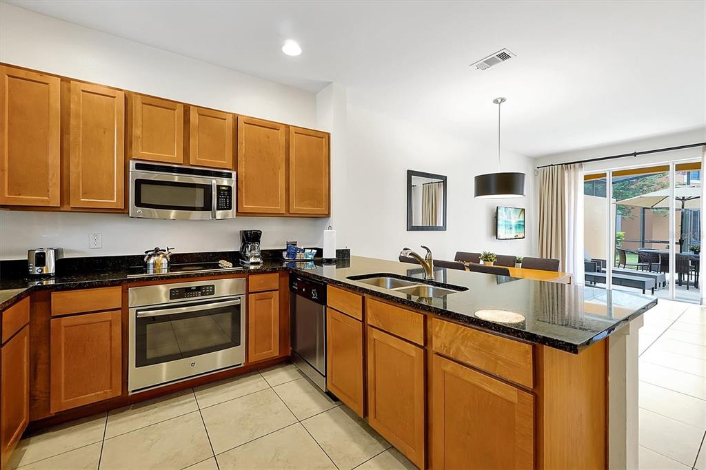 A kitchen with wood cabinets, black granite countertops, stainless steel appliances, and a dining area — 2652 CORVETTE LANE, KISSIMMEE, FL