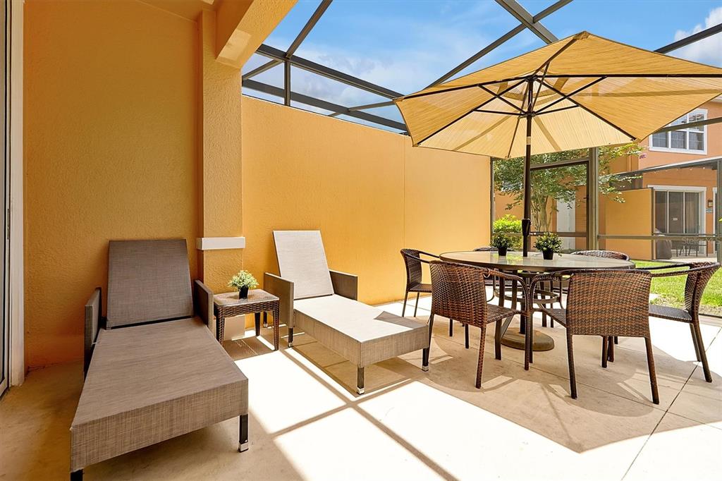 A covered patio features two lounge chairs, a dining set with an umbrella, and screens — 2652 CORVETTE LANE, KISSIMMEE, FL