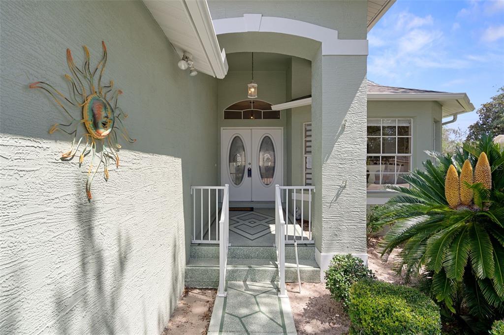 A light green house exterior features a double front door, white railings, and a sun decoration — 7483 BRIDGEWATER LANE, SPRING HILL, FL
