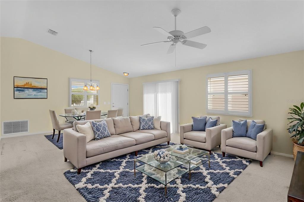 A living room with beige carpet, a blue patterned rug, and a glass coffee table — 1838 ENDSLEY COURT, THE VILLAGES, FL