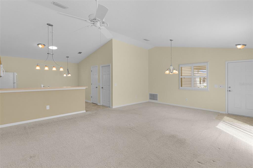 A living room with beige carpet, vaulted ceilings, a ceiling fan, and an open kitchen — 1838 ENDSLEY COURT, THE VILLAGES, FL