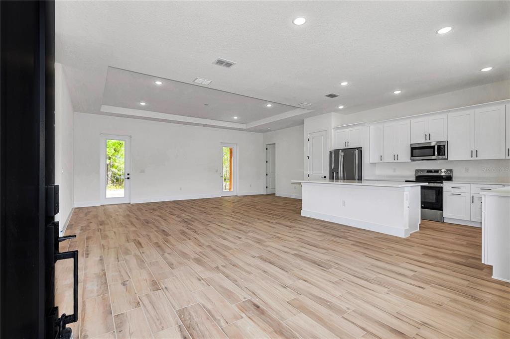 An open-concept kitchen and living area feature white cabinetry, stainless steel appliances, and wood-look flooring — 5014 SW 134TH TERRACE, OCALA, FL