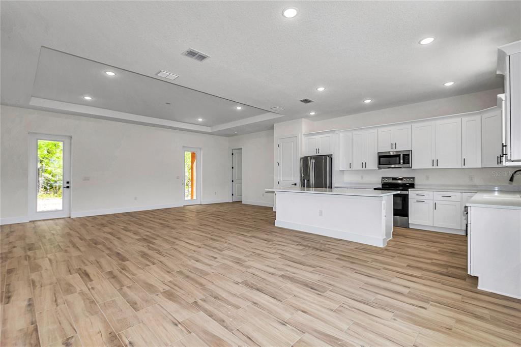 A bright, open-concept kitchen and living area with white cabinetry and wood-look tile flooring — 5014 SW 134TH TERRACE, OCALA, FL