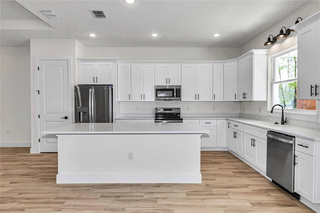 A modern kitchen features white cabinetry, stainless steel appliances, a center island, and wood-look flooring — 5014 SW 134TH TERRACE, OCALA, FL