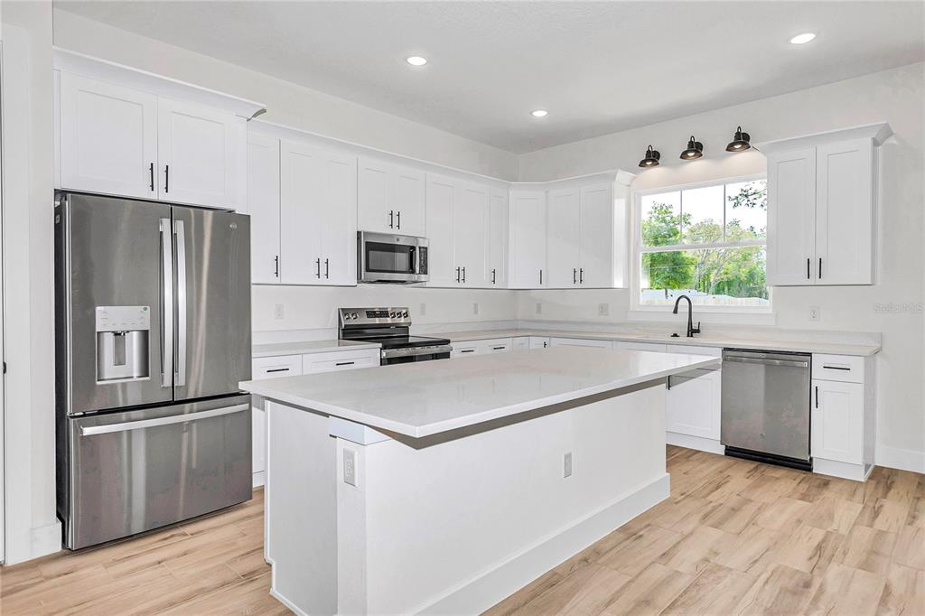 A modern kitchen features white cabinetry, stainless steel appliances, a central island, and wood-look flooring — 5014 SW 134TH TERRACE, OCALA, FL
