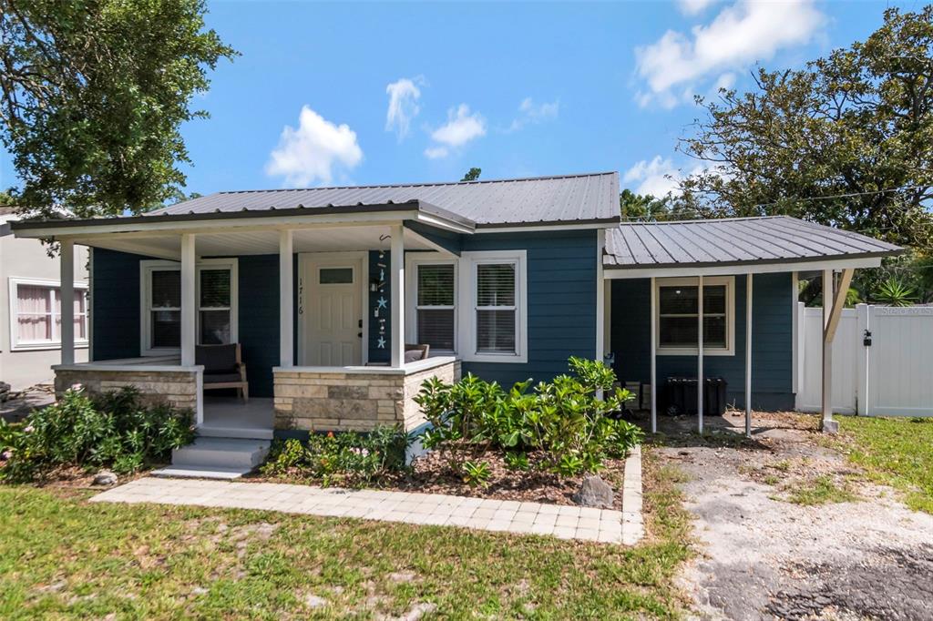 A blue house with a metal roof, front porch, and stone base sits on a lawn — 1716 W SITKA STREET, TAMPA, FL