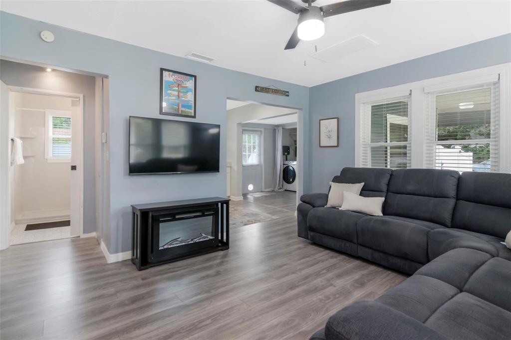 A living room features light blue walls, wood-look flooring, a dark sectional sofa, and a television — 1716 W SITKA STREET, TAMPA, FL