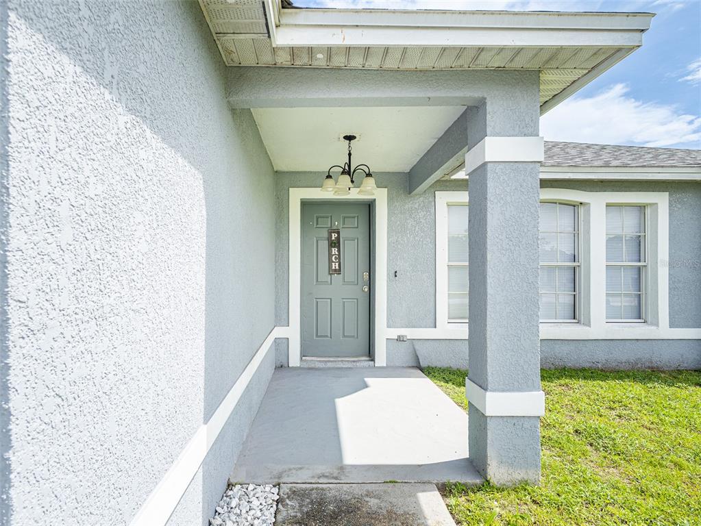A covered front porch with a gray door and a light fixture leads to the entrance — 559 HUMMINGBIRD COURT, POINCIANA, FL