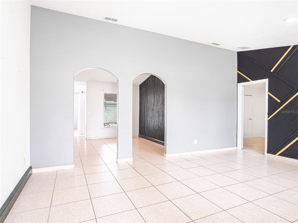 A room with light-colored tile flooring, gray walls, two arched doorways, and a black accent wall — 559 HUMMINGBIRD COURT, POINCIANA, FL