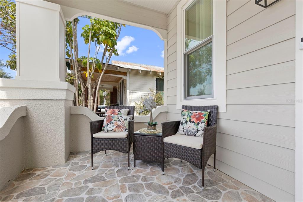 A covered porch features stone-tiled flooring, two wicker chairs with floral pillows, and a side table — 1917 W LEMON STREET, TAMPA, FL