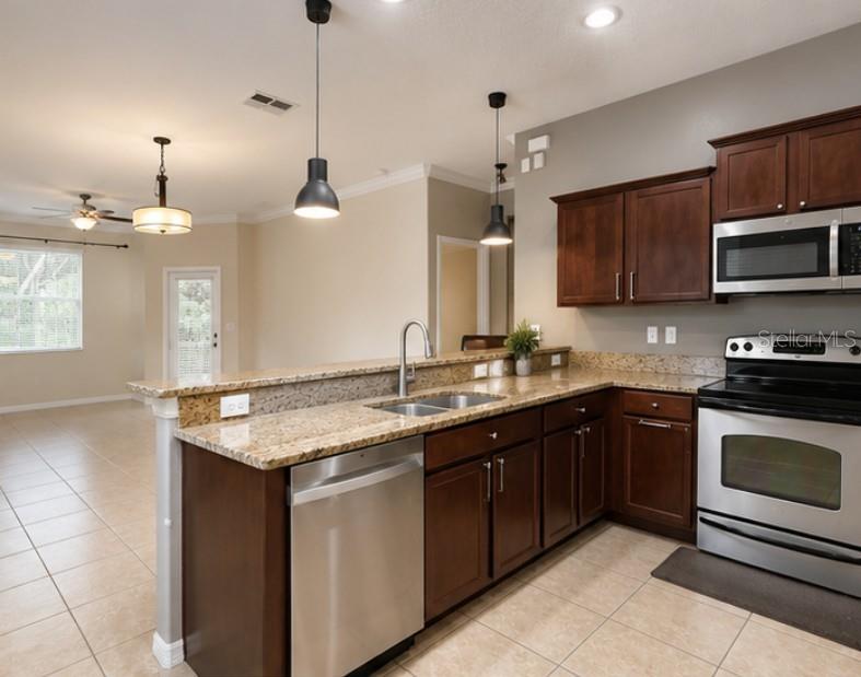 A kitchen with dark wood cabinets, granite countertops, stainless steel appliances, and pendant lighting — 8505 BROKEN WILLOW COURT, TAMPA, FL