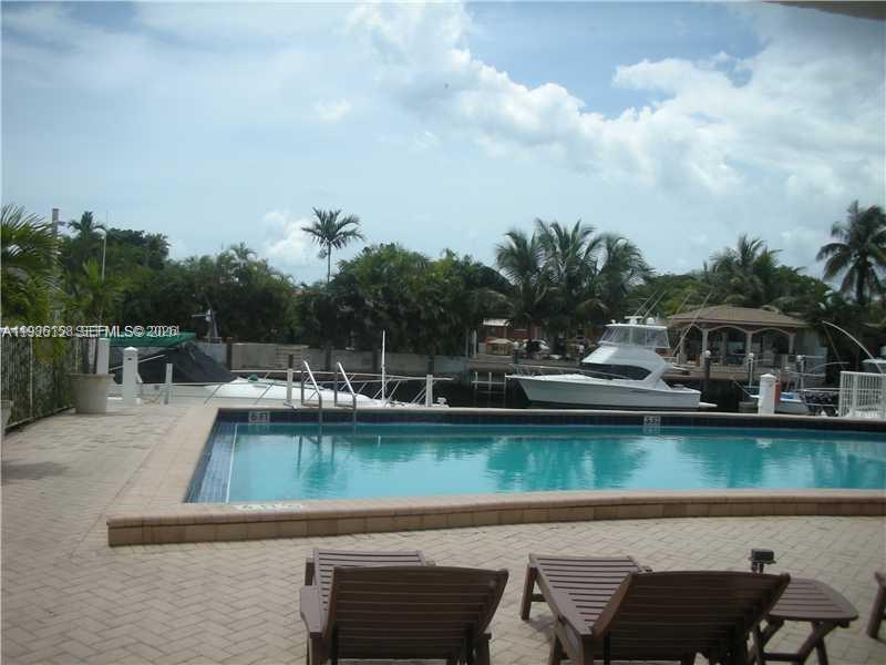 A swimming pool overlooks a canal with docked boats and palm trees under a cloudy sky — 2000 NE 135th St # 1002, North Miami FL 33181, NORTH MIAMI, FL