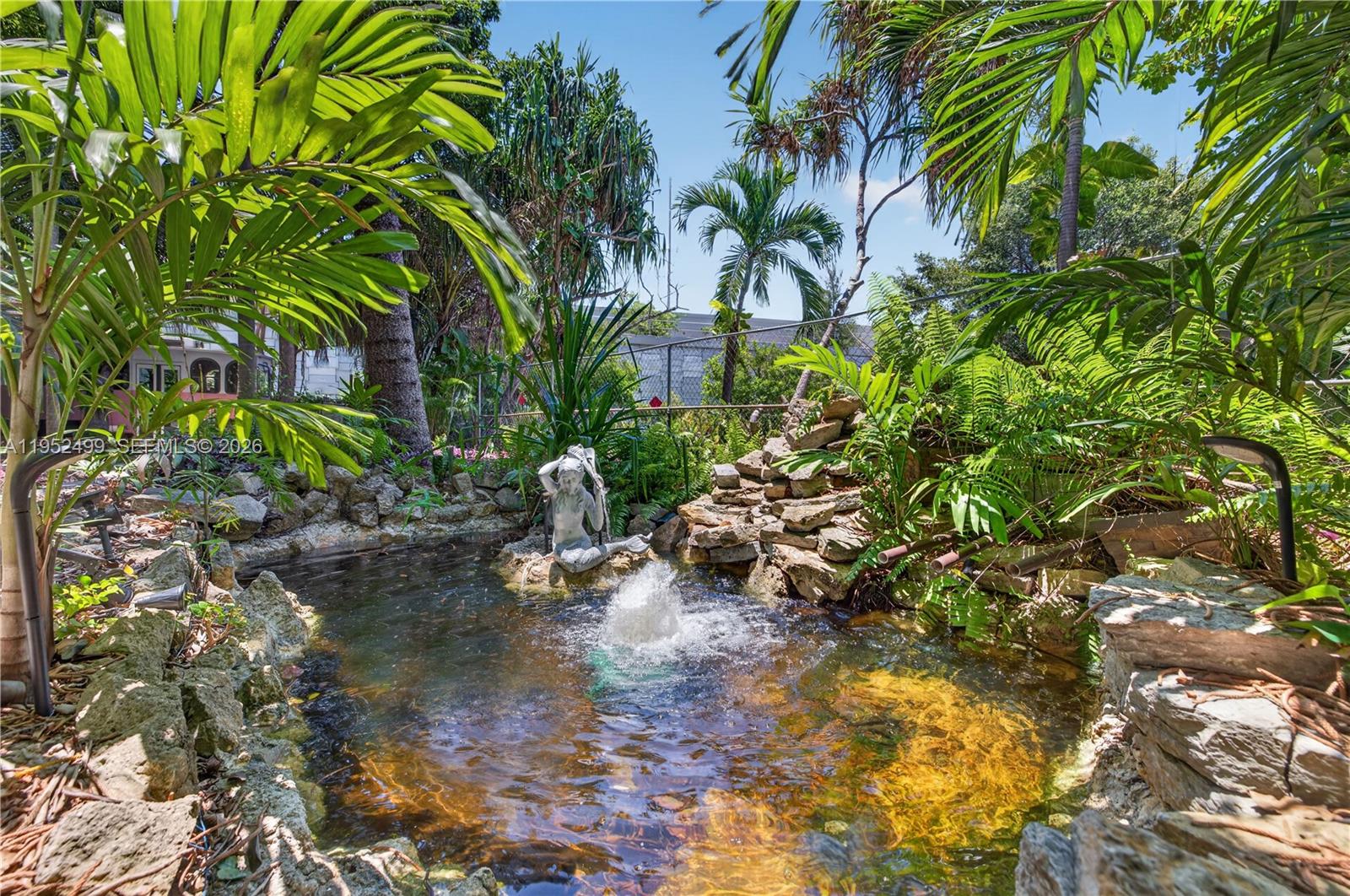 A stone-lined koi pond features a mermaid statue and a small fountain in a garden — 732 NW 43rd Ct, Oakland Park FL 33309, OAKLAND PARK, FL