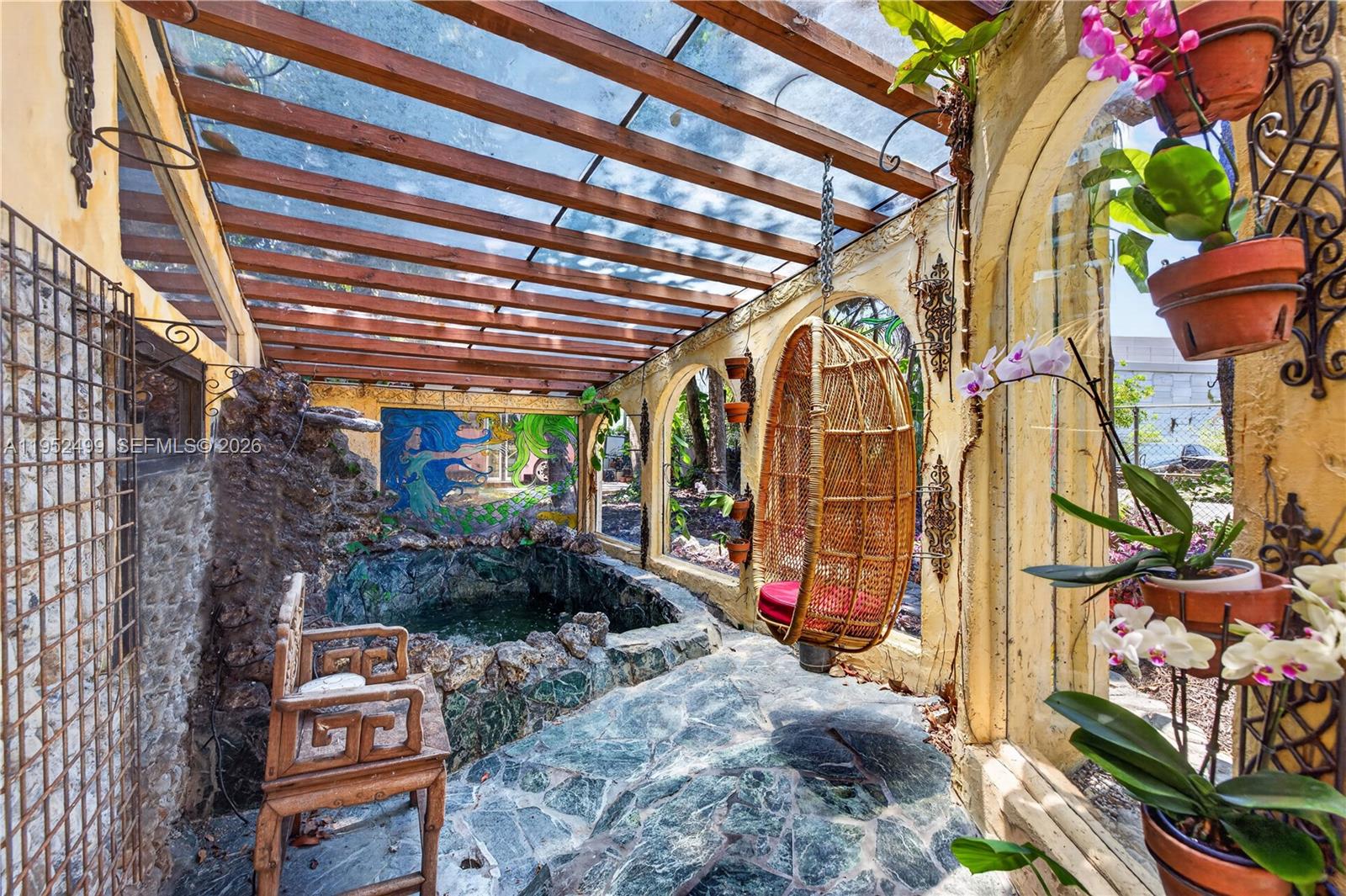 A sunroom features a stone-lined pond, a hanging wicker chair, and a wooden pergola roof — 732 NW 43rd Ct, Oakland Park FL 33309, OAKLAND PARK, FL