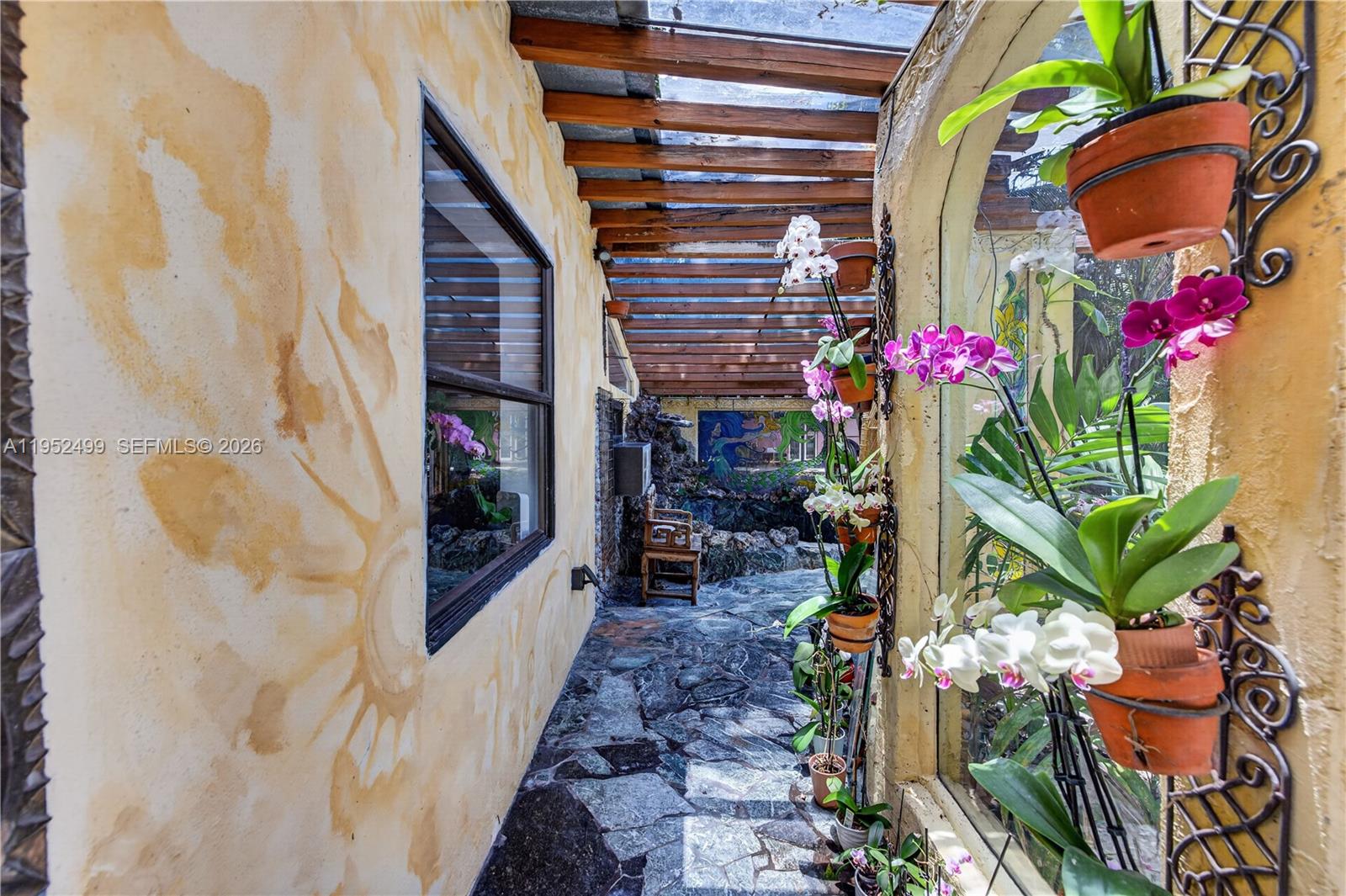 A covered outdoor walkway features stone flooring, a wooden pergola, and hanging orchid planters — 732 NW 43rd Ct, Oakland Park FL 33309, OAKLAND PARK, FL