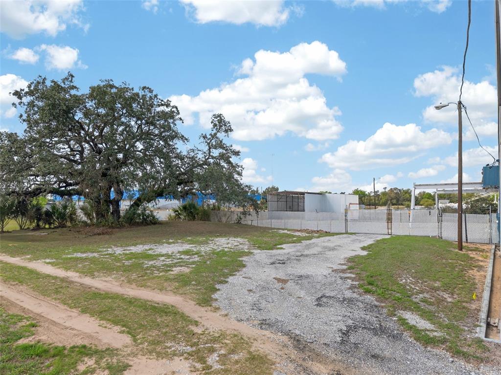 A gravel driveway leads to a fenced lot with a large tree under a blue sky — HWY 17 92 N, HAINES CITY, FL