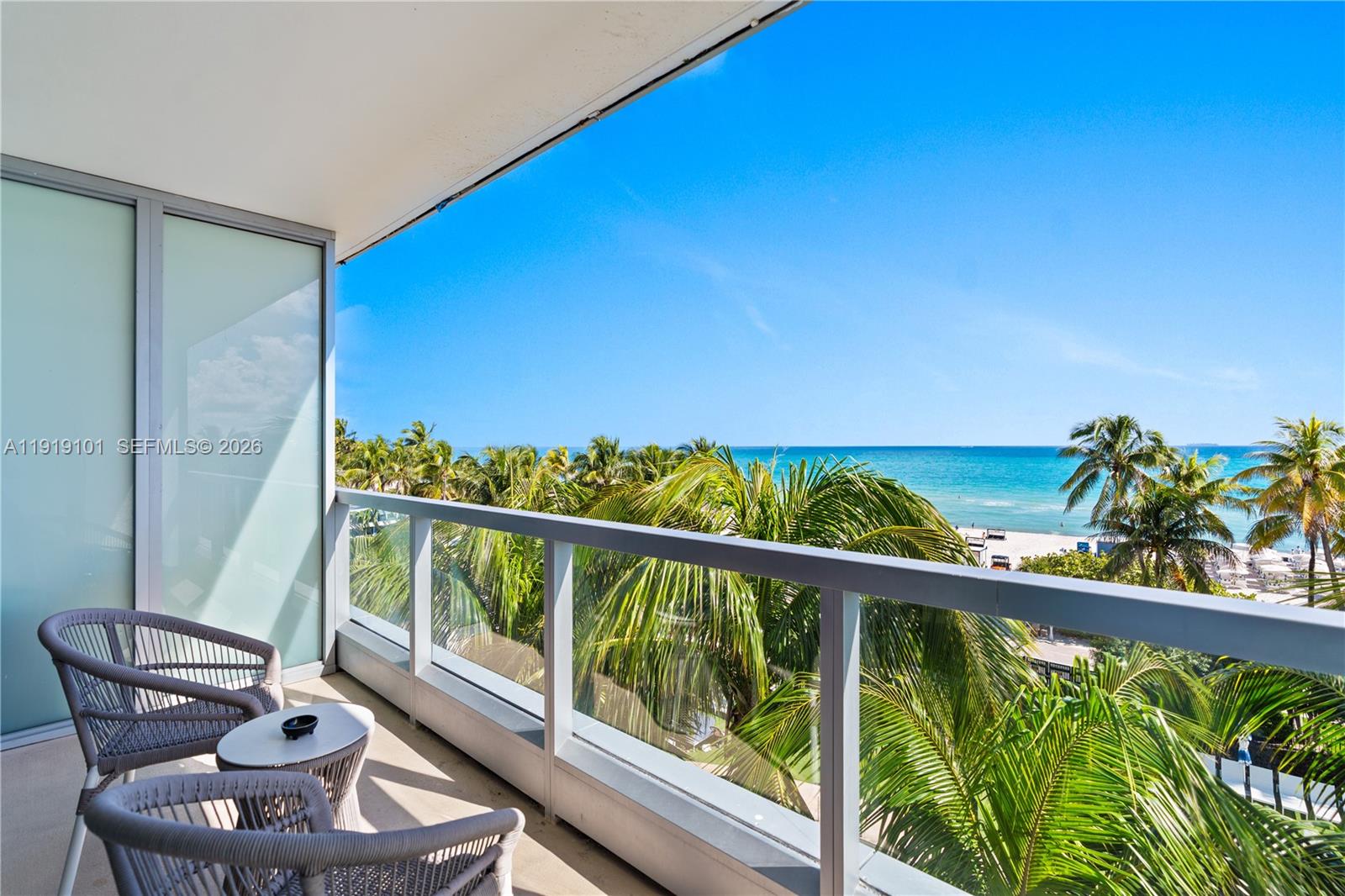 A balcony with two chairs and a small table overlooks palm trees and the ocean — 4391 Collins Ave # 413, Miami Beach FL 33140, MIAMI BEACH, FL