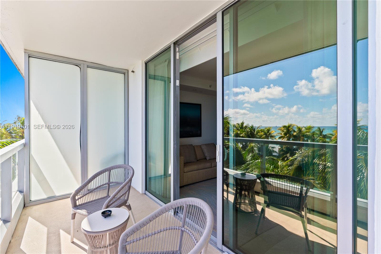 A balcony features two chairs, a small table, and sliding glass doors overlooking palm trees — 4391 Collins Ave # 413, Miami Beach FL 33140, MIAMI BEACH, FL
