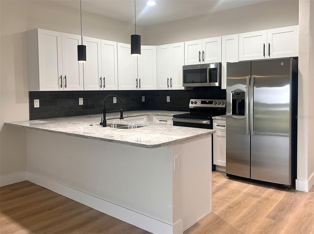 A kitchen features white cabinets, granite countertops, a black tile backsplash, and stainless steel appliances — 7214-7216 DAVID BOULEVARD, PORT CHARLOTTE, FL