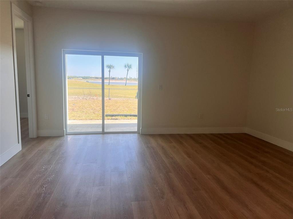 An empty room features light wood-look flooring, neutral walls, and a sliding glass door — 7214-7216 DAVID BOULEVARD, PORT CHARLOTTE, FL