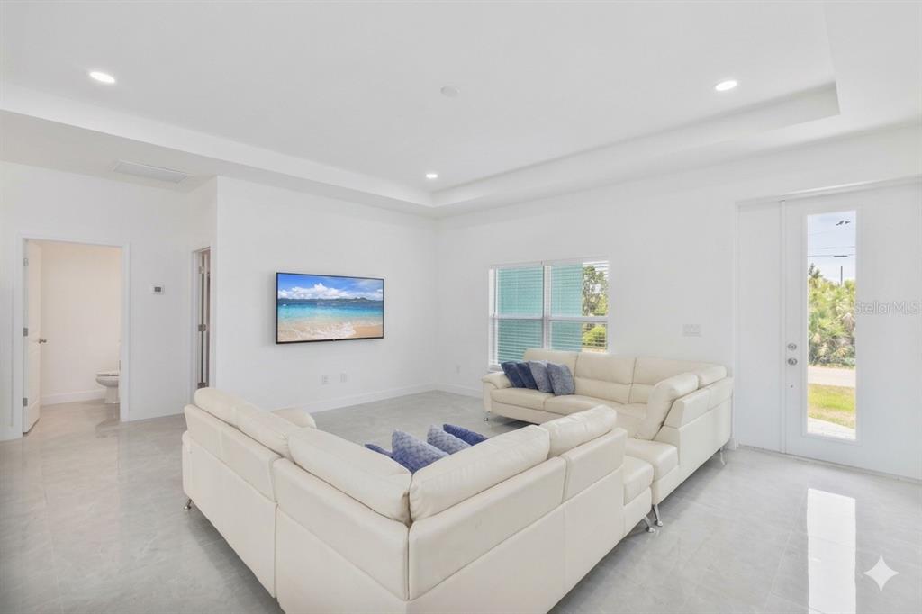 A bright living room features white tile floors, a large sectional sofa, and a television — 15473 LAKELAND CIRCLE, PORT CHARLOTTE, FL