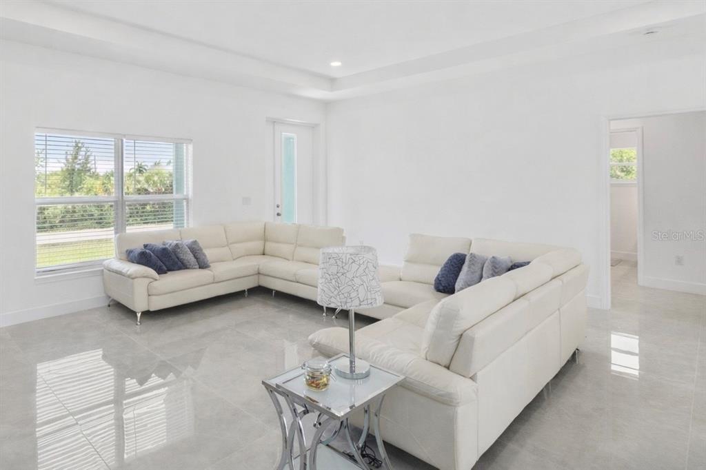 A spacious living room features white leather sectional sofas, large windows, and light-colored tile flooring — 15473 LAKELAND CIRCLE, PORT CHARLOTTE, FL