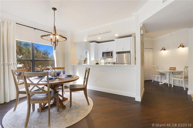 A dining area with a round wooden table and chandelier sits beside an open kitchen — 100 Uno Lago Drive # 205, Juno Beach FL 33408, JUNO BEACH, FL