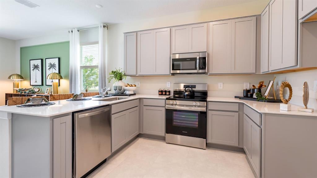 A modern kitchen features light gray cabinets, stainless steel appliances, and white quartz countertops — 5844 ENERGY WAY, CLERMONT, FL