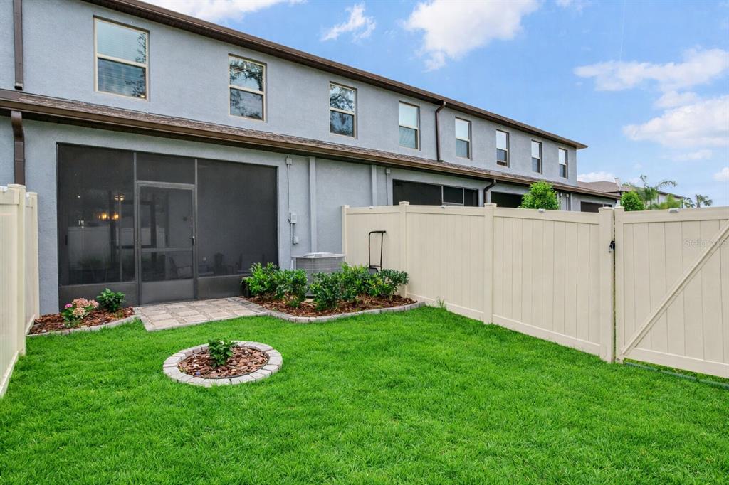 A fenced backyard with a small lawn, a screened patio, and a stone garden bed — 2561 CHARLAN COURT, HOLIDAY, FL