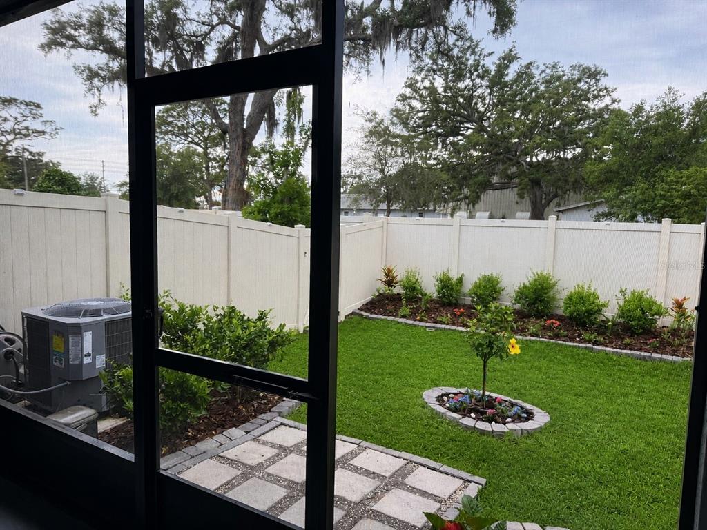 A view of a fenced backyard with a small patio, lawn, and landscaping from a screen — 2561 CHARLAN COURT, HOLIDAY, FL