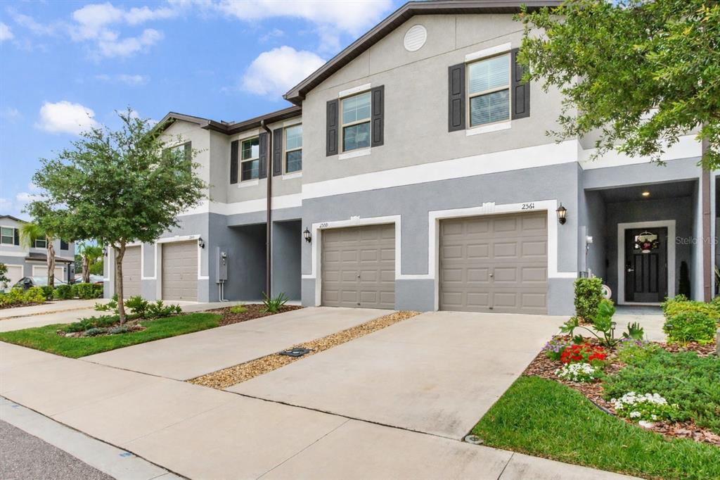 A row of two-story townhomes with gray stucco facades, concrete driveways, and attached garages — 2561 CHARLAN COURT, HOLIDAY, FL