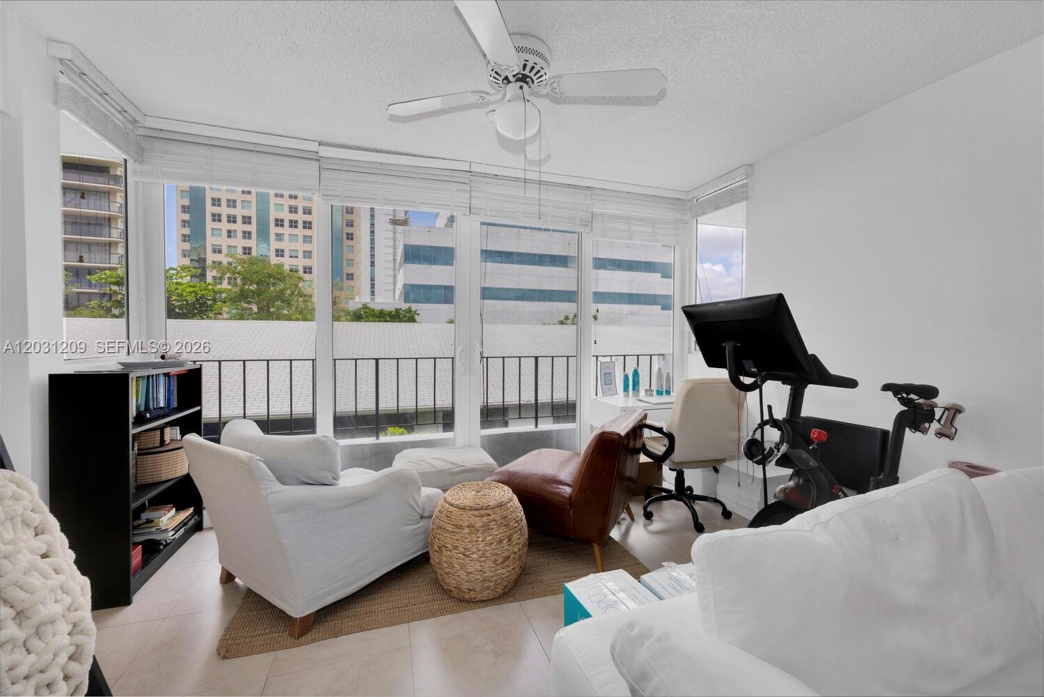 A sunlit room features a seating area, a desk, and an exercise bike by windows — 2539 S Bayshore Dr, Coconut Grove FL 33133, COCONUT GROVE, FL