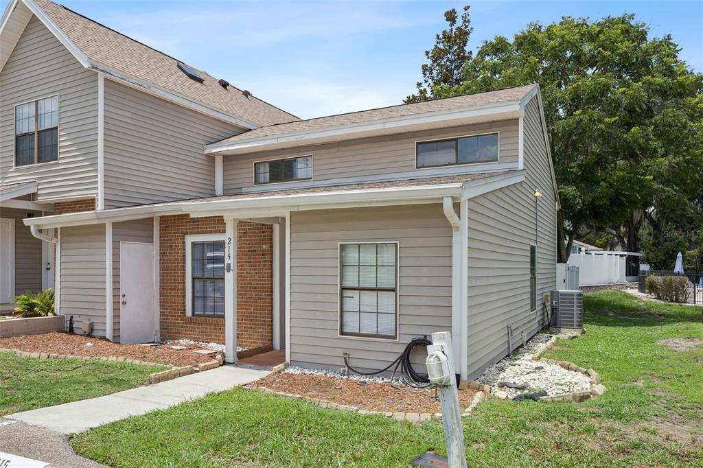 A two-story townhouse with beige siding, a brick accent wall, and a small front porch — 215 ARBOR CIRCLE, SANFORD, FL