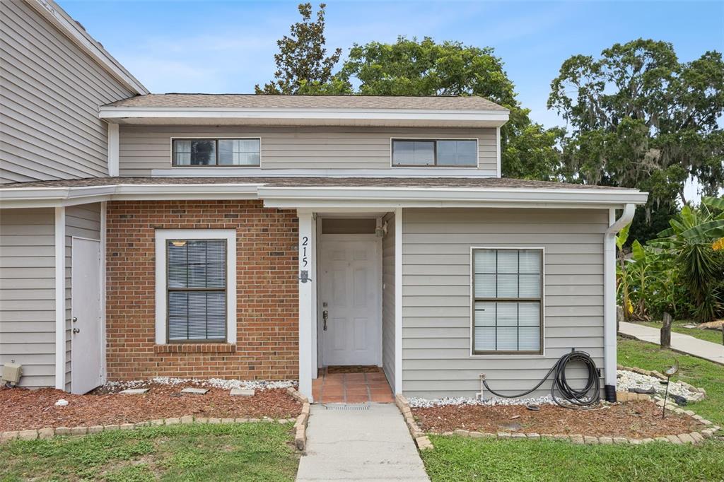 A two-story townhouse exterior features a brick facade, gray siding, and a white front door — 215 ARBOR CIRCLE, SANFORD, FL